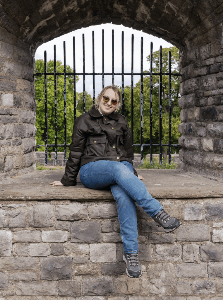 Artist sitting on stone ledge in front of iron bars and trees.